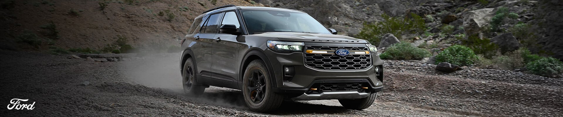 Front three-quarter view 2027 Ford Explorer Tremor in Marsh Gray kicking up dust in a rocky off-road mountain.