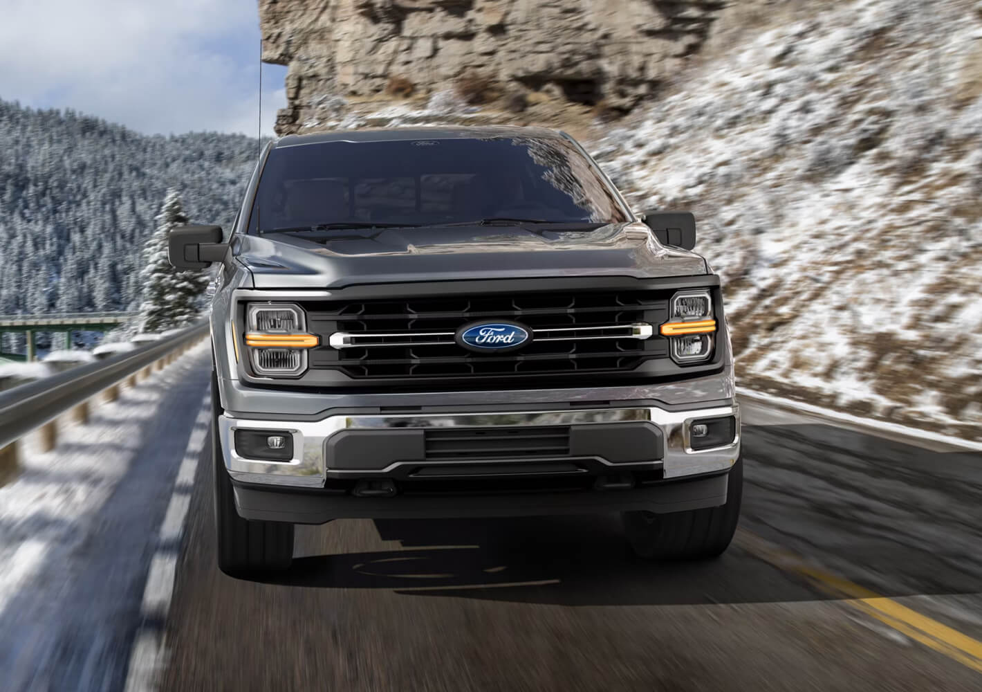 Front view of a silver Ford F-150 driving on a mountain highway.