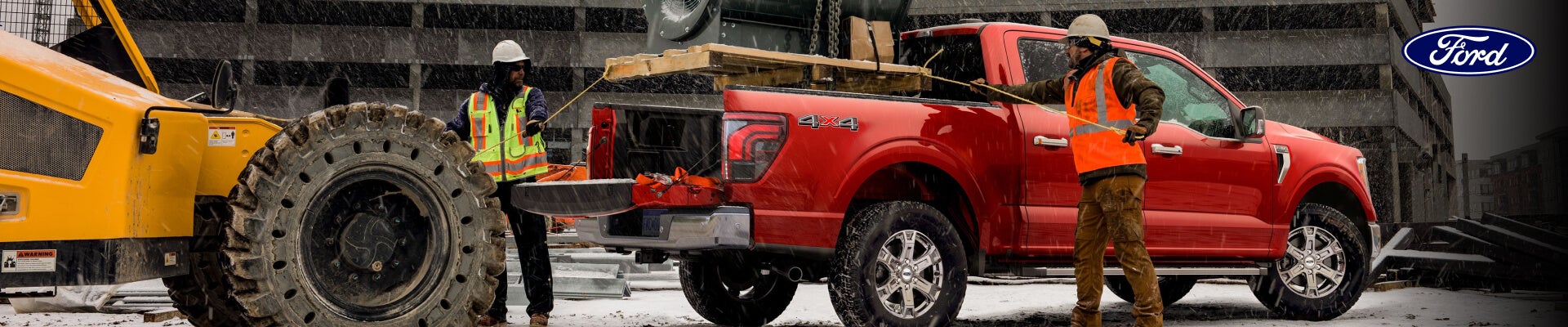 2026 Ford F-150 XLT in Ruby Red Metallic at a snowy construction site, with two workers loading the truck bed.
